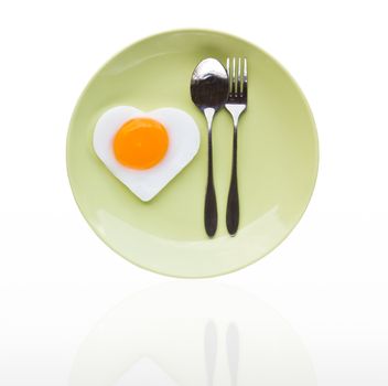 Fried egg heart and spoon on green dish