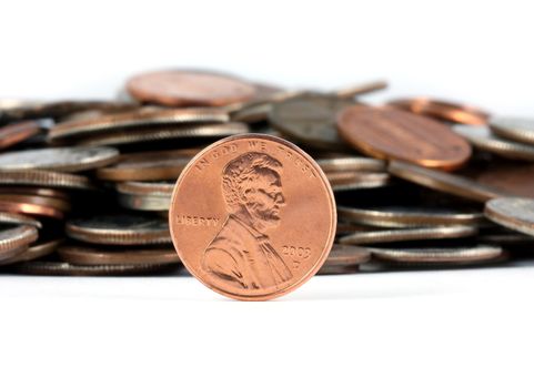 A penny standing in front of a pile of change. Shot on a white background.