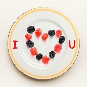 Heart from raspberry and blackberry on white plate