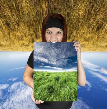 Redhead girl holding a blue sky/green field canvas. The background is upside down expressing a concept of travel dreams.

Shot in studio. Composite background.