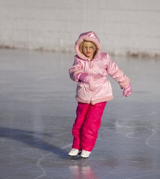 Child in pink ice skating and leaning into a curve