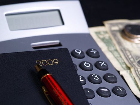 Calculator, calendar, pen and dollar over black