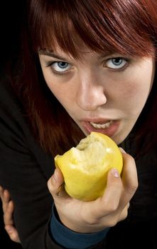 Redhead girl biting a yellow apple with a seductive and attractive look.