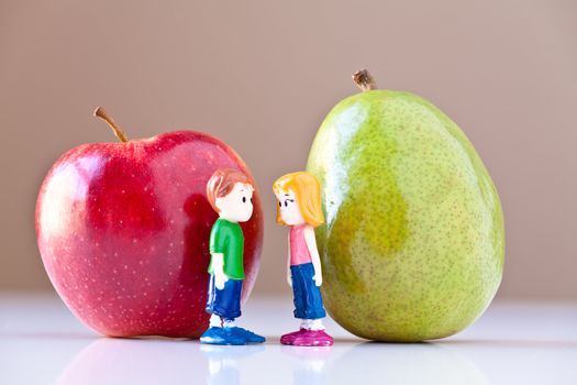 Toy girl and boy discuss nutrition and healthy choices in front of a green pear and a  red apple. The concepts depicted in this image are nutrition, good food choices, balanced diet and good for you.