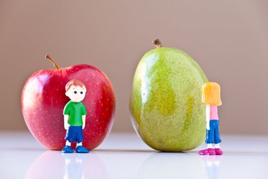 Toy girl and boy disagree over nutrition and healthy choices in front of a green pear and a  red apple. The concepts depicted in this image are nutrition, good food choices, balanced diet and good for you.