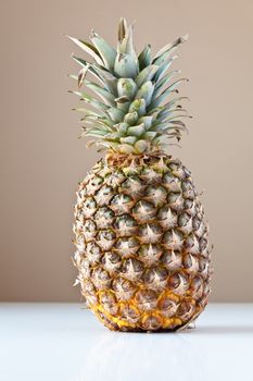 Single partially ripened pineapple on white table with taupe brown background. The concepts depicted in this image are nutrition, good food choices, balanced diet and good for you.