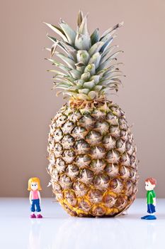 Toy girl and boy are overwhelmed by nutrition and healthy choices next to a giant pineapple. The concepts depicted in this image are nutrition, good food choices, balanced diet and good for you.