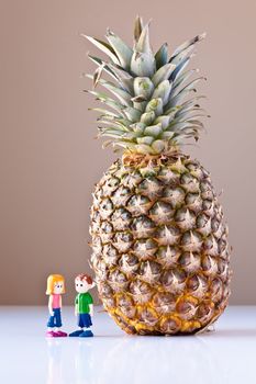 Toy girl and boy discuss nutrition and healthy choices next to a giant pineapple. The concepts depicted in this image are nutrition, good food choices, balanced diet and good for you.