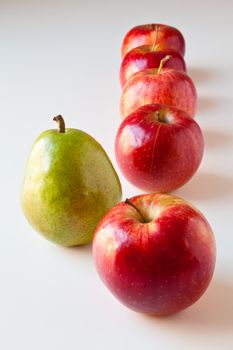 Green pear standing out from a line of red apples. The concepts depicted in this image are nutrition, good food choices, balanced diet, good for you, being different, unique, stick out, being singled out.