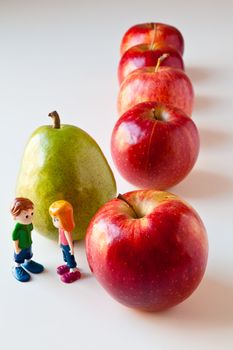 Toy girl and boy discuss nutrition and healthy choices in front of green pear standing out from a line of red apples. The concepts depicted in this image are nutrition, good food choices, balanced diet, good for you, being different, unique, stick out, being singled out.