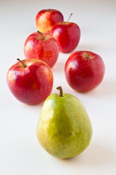 Green pear leading a group of red apples. The concepts depicted in this image are nutrition, good food choices, balanced diet, good for you, being different, unique, stick out, being singled out, leading by example.