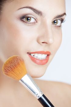 Smiling lady with makeup brush on a studio background