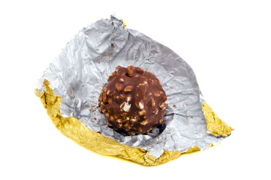 Candy coated with chocolate and nuts rolled out of golden paper isolated on a white background.