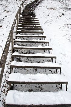 Stairs covered with snow leading to a steep hill in winter.