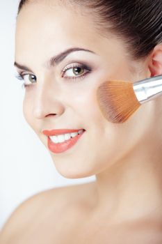 Smiling lady applies makeup brush on a studio background