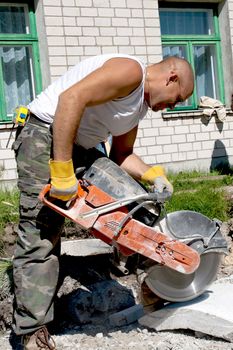Shot of a construction road worker cutting a paving stone whit a industrial petrol power cutter on a construction site