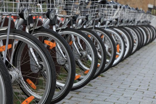 Row of city bicycles parked in a paved street.Selective focus on the first wheel.