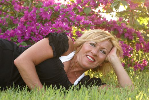 A woman lays on the grass next to some bougainvillea flowers.