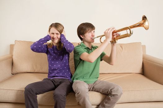 Photo of a brother playing his trumpet too loudly, or badly, and annoying his sister.