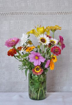 A bouquet of garden flowers in a glass jar on the background of an old linen canvas. August, the Central Russia