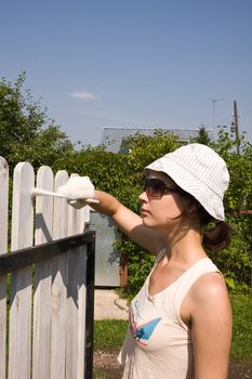 Beautiful girl colours the wooden fence