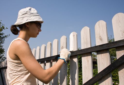 Beautiful girl colours the wooden fence