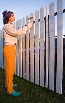 Beautiful girl colours the wooden fence