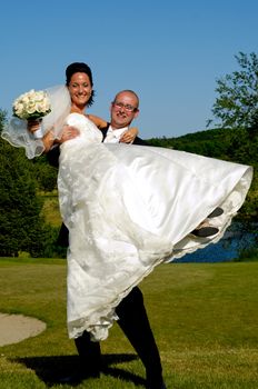 Groom is lifting his bride up in a park.