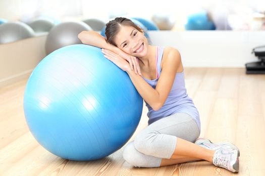 Fitness woman in gym resting on pilates ball / exercise ball after training. Beautiful multiracial fitness model in gym.