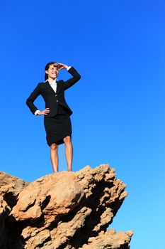 Business woman looking from mountain top. Business future concept image - businesswoman looking at horizon. Young multiracial executive.