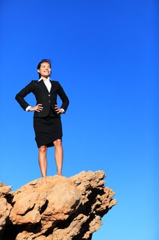 Success and challenges - business concept image. Successful business woman reaching goals overcoming challenges and adversity standing on mountain top in suit.