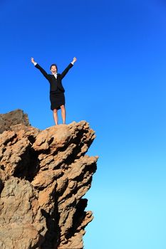 Business success concept. Businesswoman on top of mountain winning overcoming adversity and challenges. Successful young multiracial business woman in suit outdoors in nature.