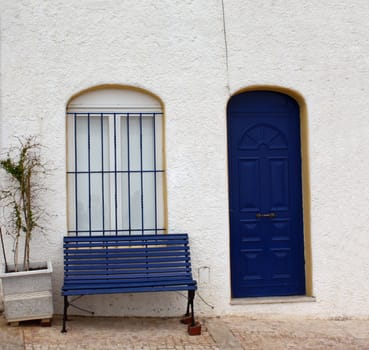 Typical whitewashed Portuguese house with blue door and blue bench outside.