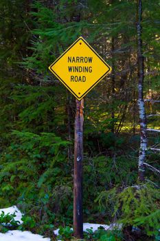 A yellow caution signs warns of a narrow and winding road ahead for drivers in this forest in the winter.