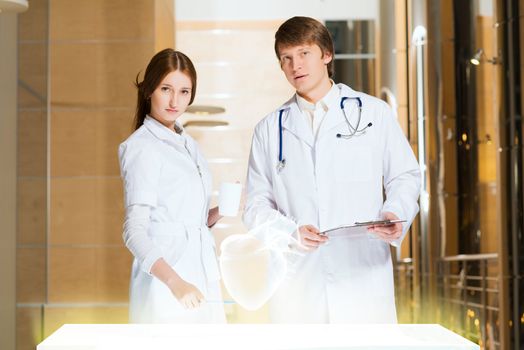 two doctors stand near glowing table discussing. projected objects on a desk