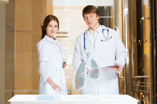 two doctors stand near glowing table discussing. projected objects on a desk