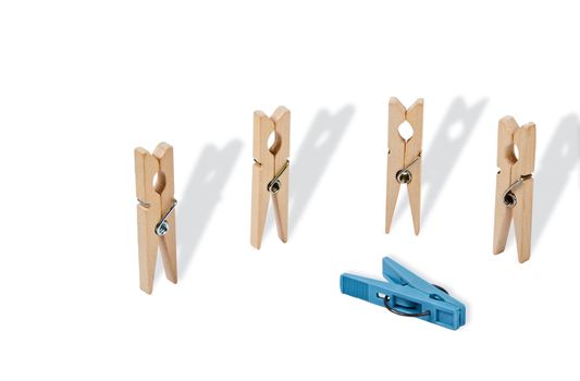 Abstract act of violence. Closeup of four white wooden pegs are vertical position, horizontally near them is a plastic clothespin blue. Long shadows emphasize the situation. File includes a clipping path.