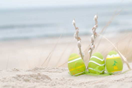 Easter decorated eggs and catkin on sand. Beach and ocean in the background