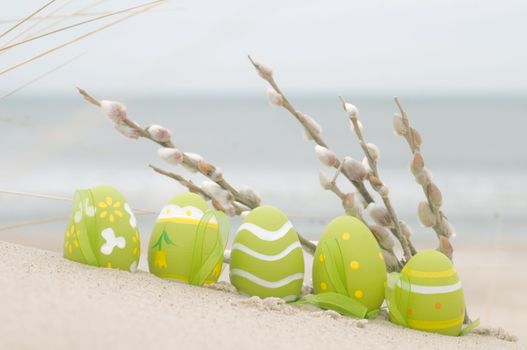 Easter decorated eggs and catkin on sand. Beach and ocean in the background