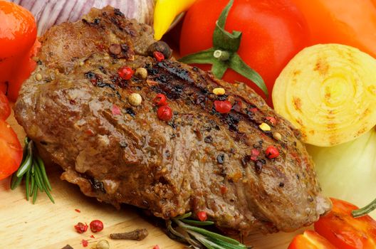 Grilled Beef and Vegetables with Spices, Peppercorns, Onion, Tomatoes and Herbs closeup on Wooden Board 