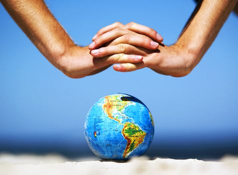 Earth globe on the beach and hands over it. Ideal for Earth protection concepts, recycling, world issues, enviroment themes