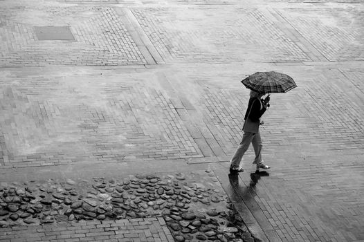 Woman with umbrella walking through rainy square