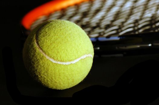 Tennis equipment - ball and racket on black. Soft light, shallow depth of field.