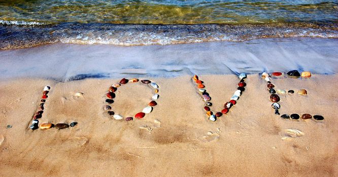 Word LOVE on beach sand, made from rocks