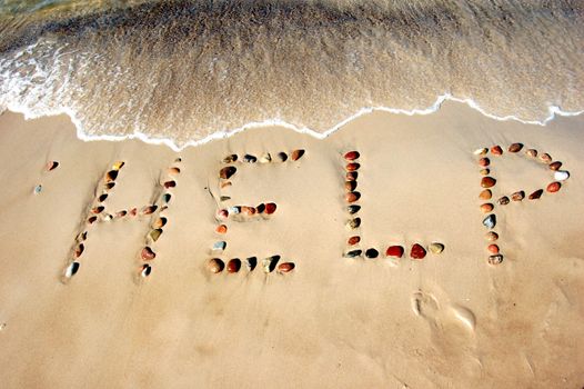 Word HELP on beach sand, made from rocks