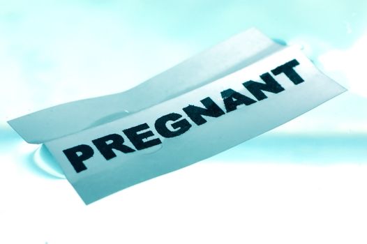 Card floating on water surface with printed word: PREGNANT 