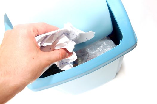 A man's hand holding a crumpled paper over a trash bin. Isolated on a white background.