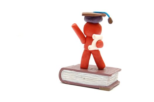 Plasticine figure celebrating graduation with certificate and student hat staying on book