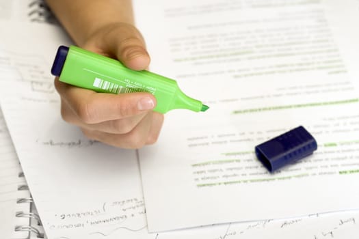 Closeup of a hand of a student using a green marker while studying.