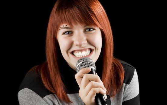 Redhead girl using her microphone singing karaoke and smiling big time.

Studio shot.